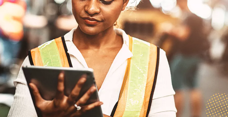 imagem de uma mulher com colete de segurança apoiando um tablet em sua mão