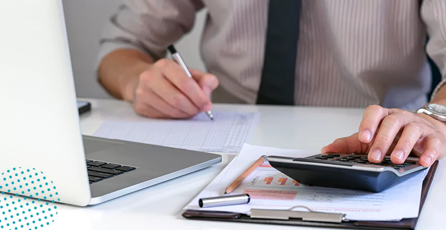 imagem de uma pessoa com calculadora, caneta, papel e um notebook na frente, realizando o cálculo correto de horas extras e adicionais