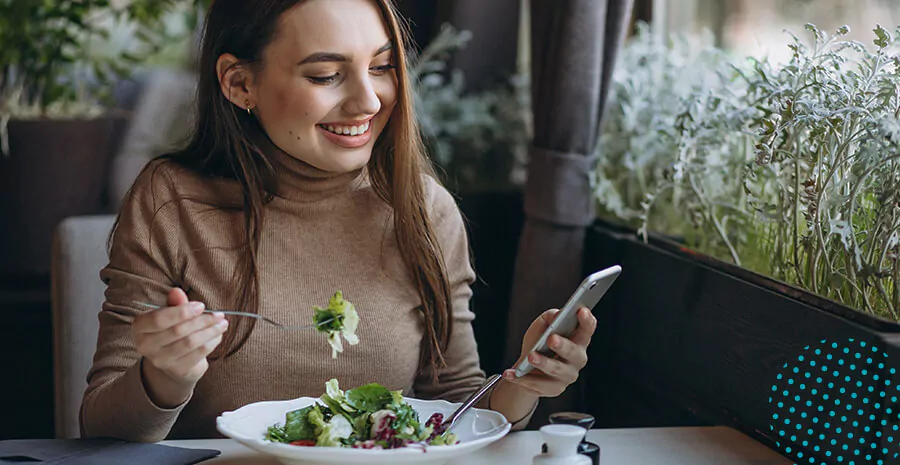 imagem de uma mulher fazendo uma refeição e sorrindo para o celular