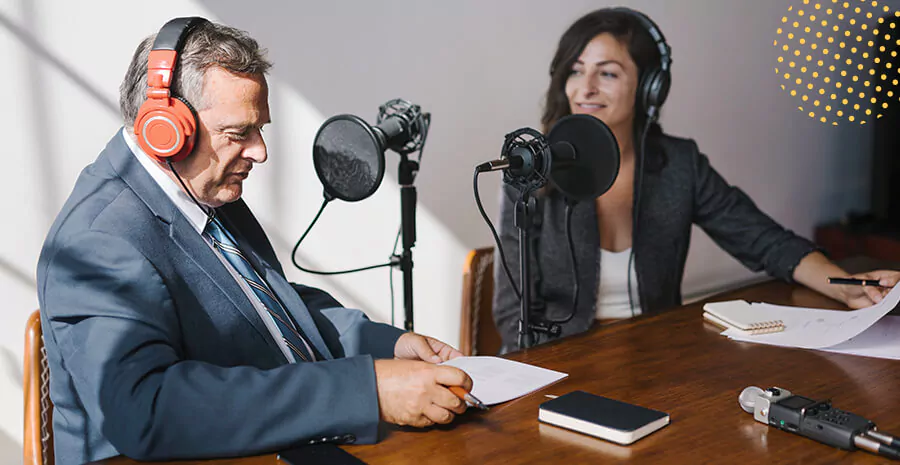 imagem de duas pessoas em uma mesa com microfones de rádio