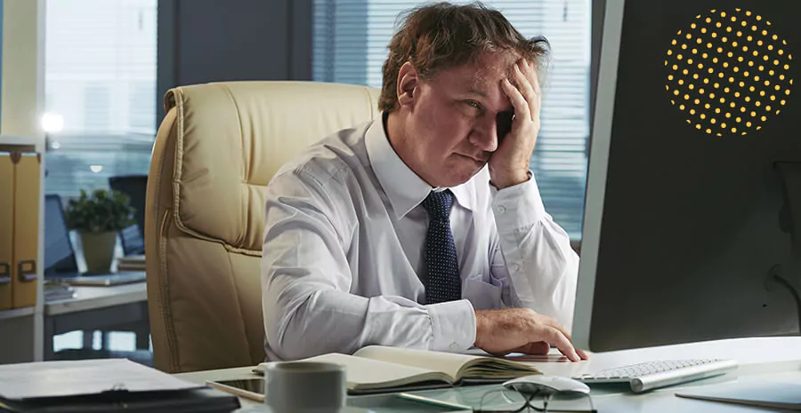 imagem de um homem em frente ao computador com um semblante de cansaço representando a síndrome de burnout