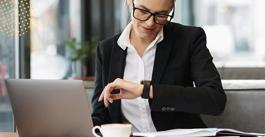 Imagem de uma mulher trabalhando em um computador e olhando o relógio no pulso