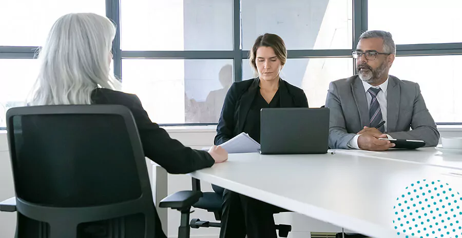 imagem de uma mulher sentada em uma cadeira de costas e duas pessoas na frente com uma mesa e notebook falando com ela