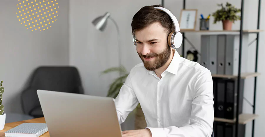 imagem de um homem sorrindo, com fones de ouvido e mexendo no notebook em home office
