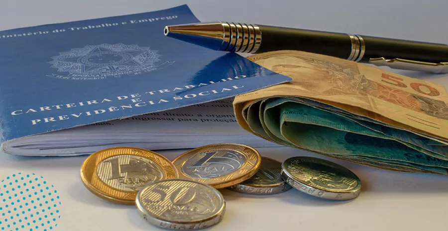 imagem da carteira de trabalho física com uma caneta, notas de dinheiro e moedas de cinquenta centavos e de um real