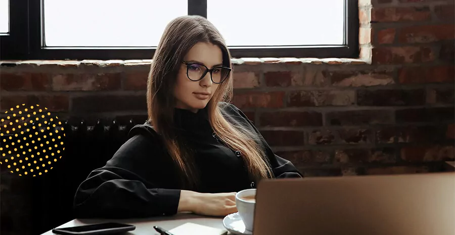 imagem de uma mulher com cara séria sentada na frente de um computador com uma xícara de café
