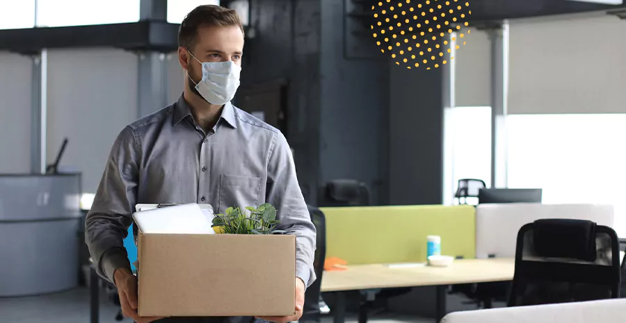 imagem de um homem usando máscara e segurando uma caixa de papelão com seus pertences em um escritório