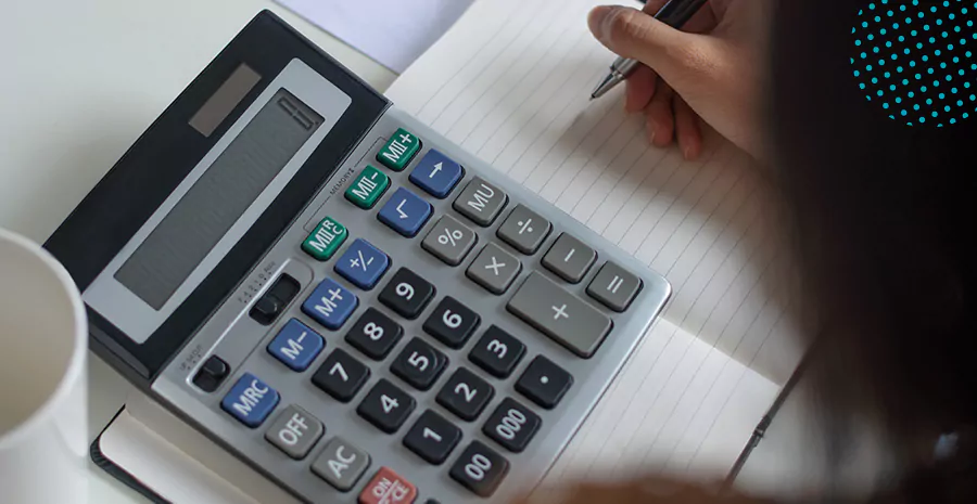 imagem de uma pessoa escrevendo em um caderno com uma calculadora do lado