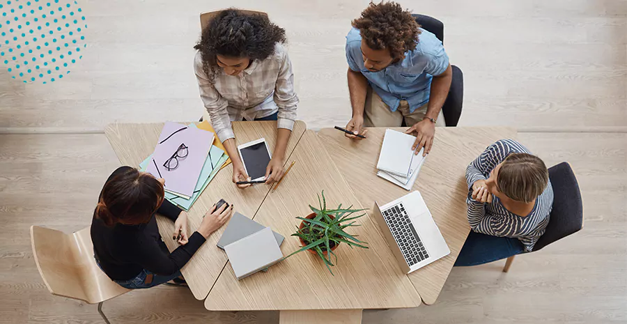imagem de um grupo de pessoas sentado ao redor de uma mesa usando celulares e computadores
