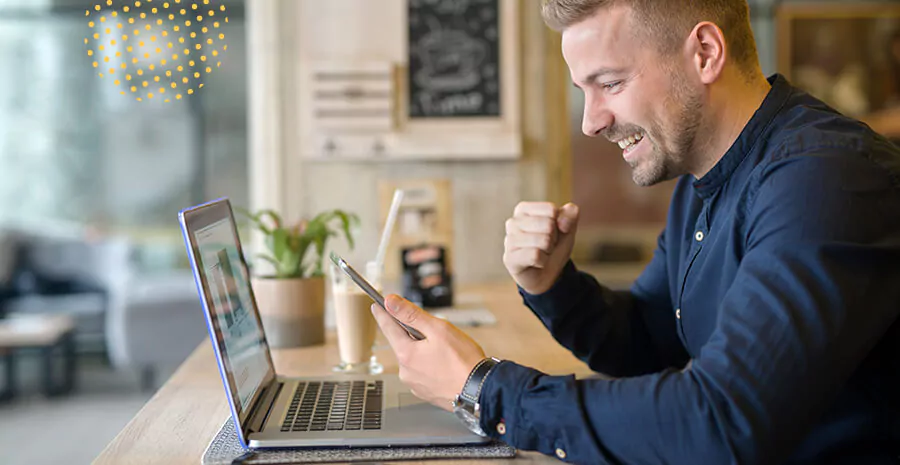 imagem de um homem sorrindo olhando para o celular com um computador na frente