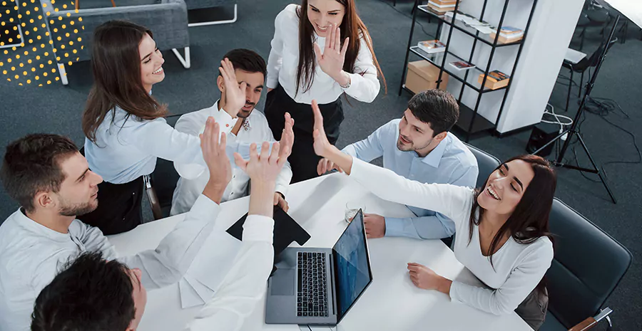 imagem de um grupo de pessoas sentado ao redor de uma mesa erguendo as mãos no centro