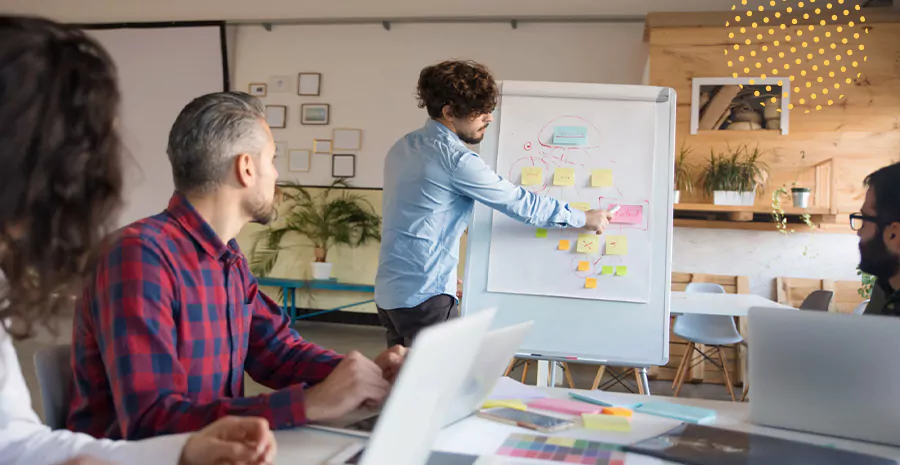 imagem de um grupo de pessoas olhando para um homem em pé na frente de um quadro branco com post its