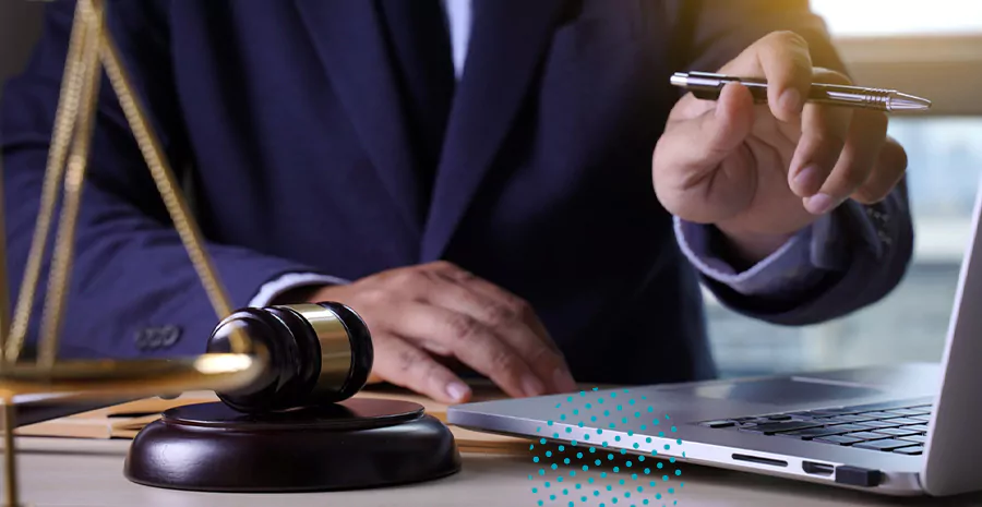imagem de um homem sentado na frente do computador segurando uma caneta e com um martelo de juiz ao lado
