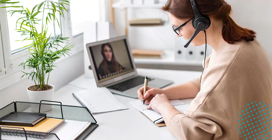 imagem de uma mulher fazendo chamada de vídeo pelo computador e escrevendo em um caderno