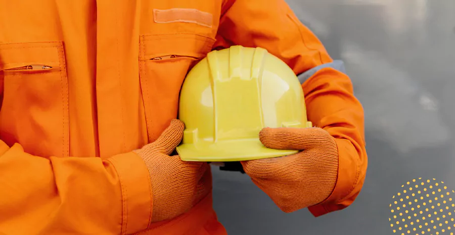 imagem de uma pessoa usando macacão de proteção e segurando um capacete amarelo de proteção