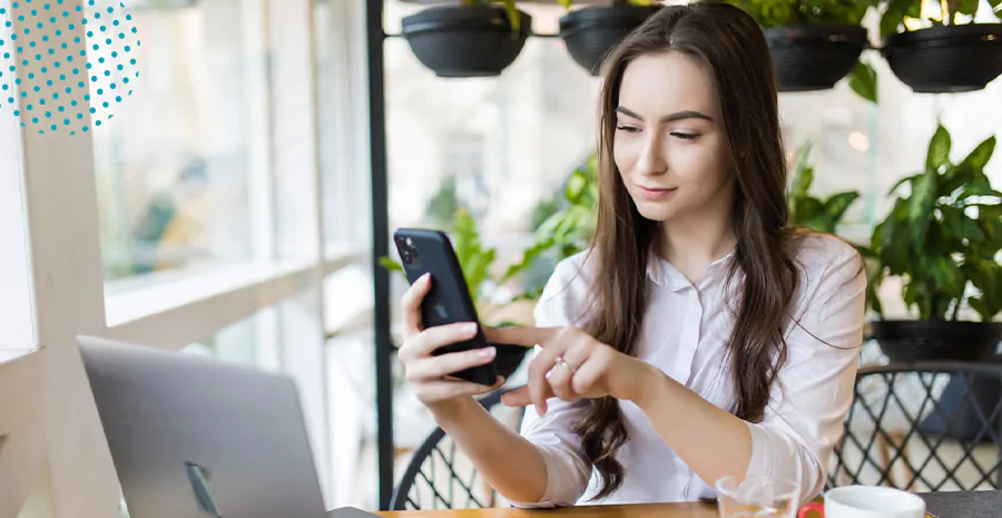 imagem de uma mulher sentada na frente de um computador e segurando um celular