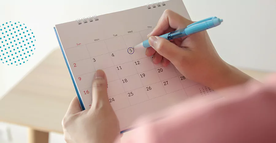 imagem de uma pessoa segurando um calendário e marcando uma data com uma caneta