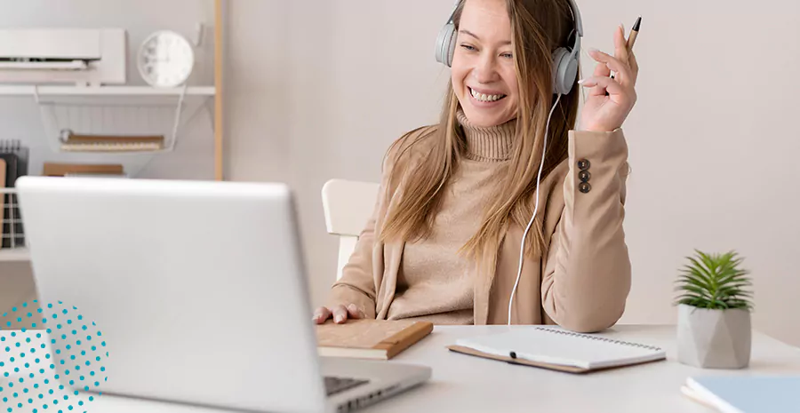 imagem de uma mulher sorrindo sentada na frente de um computador e segurando uma caneta