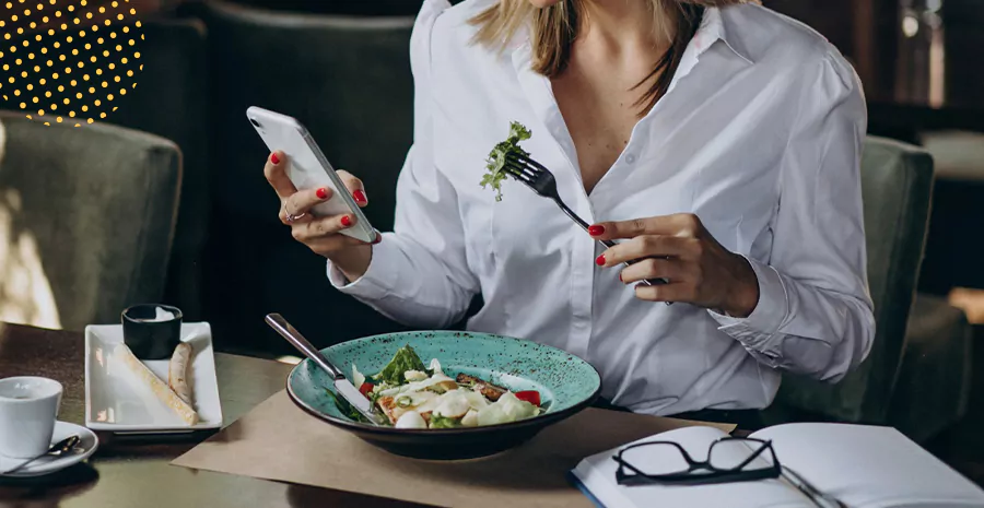 imagem de uma mulher sentada comendo salada e segurando um celular