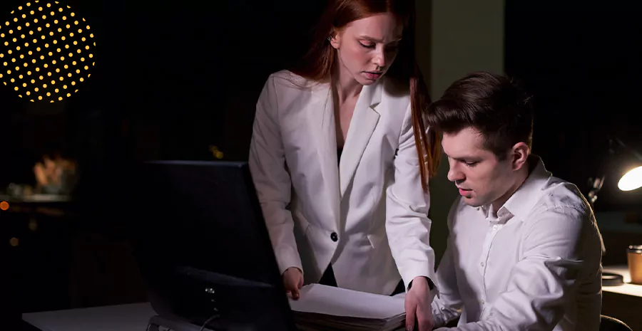 imagem de um homem sentado na frente de um computador e uma mulher em pé ao seu lado