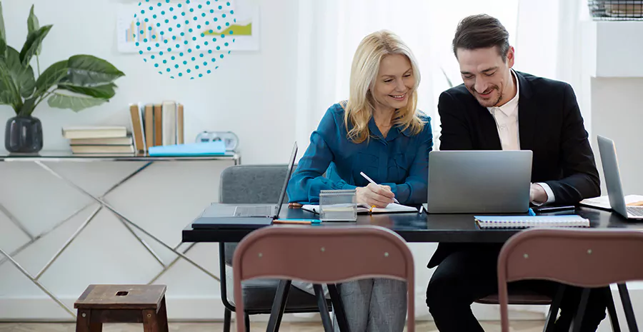 imagem de um homem e uma mulher sentados em uma mesa sorrindo e olhando para um computador