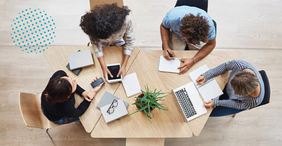 imagem de quatro pessoas sentadas ao redor de uma mesa mexendo em computadores e celulares