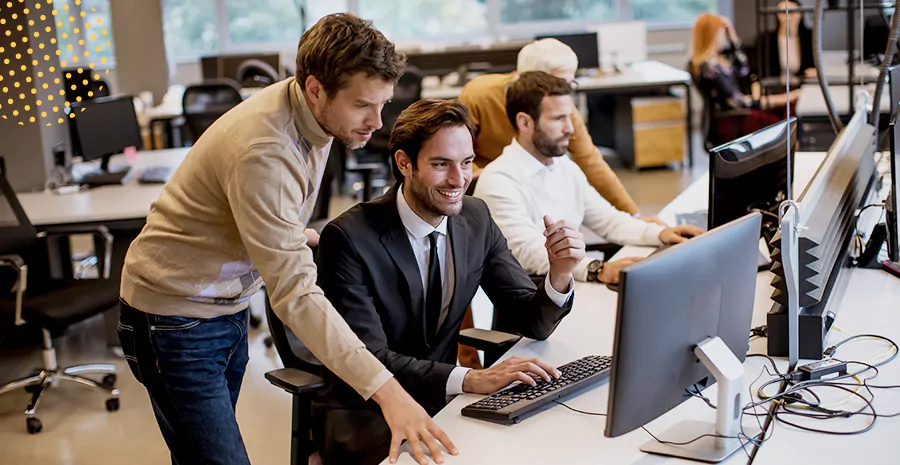 imagem de um homem em pé ao lado de outro homem sentado olhando para um computador