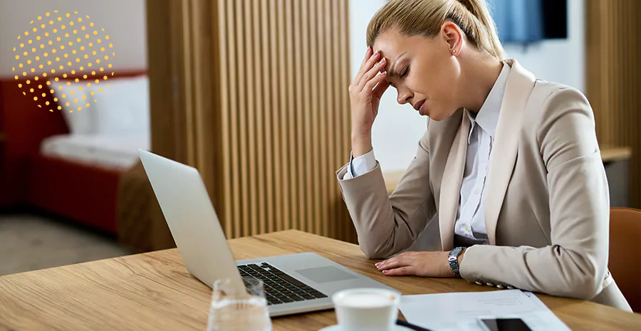 imagem de uma mulher sentada na frente de um computador cansada com a mão na testa