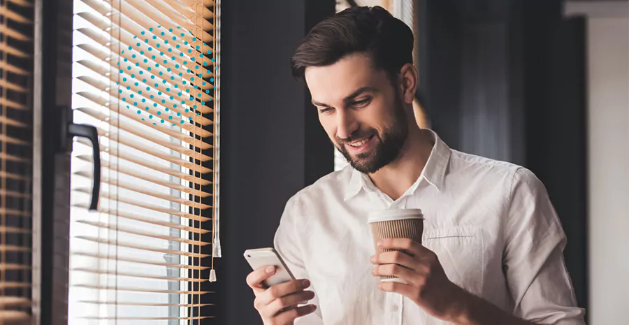 imagem de um homem sorrindo segurando um celular e um café