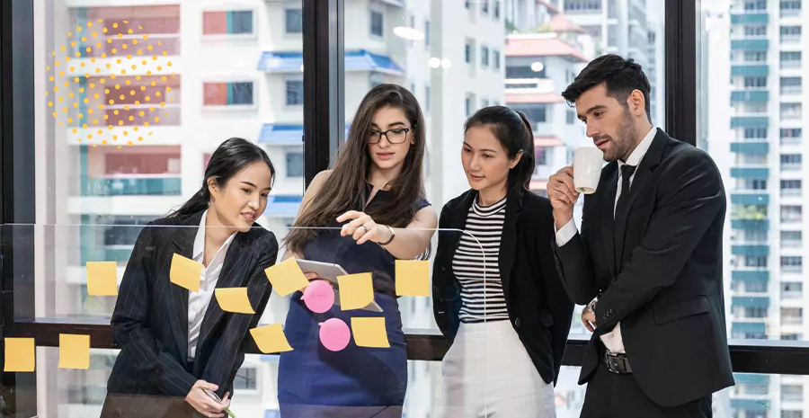 imagem de três mulheres e um homem olhando para um painel com postits colados