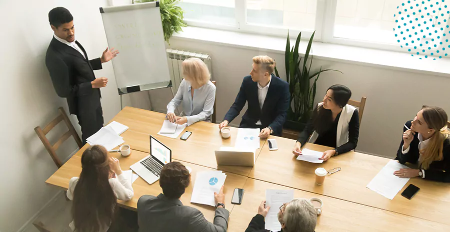 imagem de um homem em pé na frente de um grupo de pessoas sentado ao redor de uma mesa em um escritório