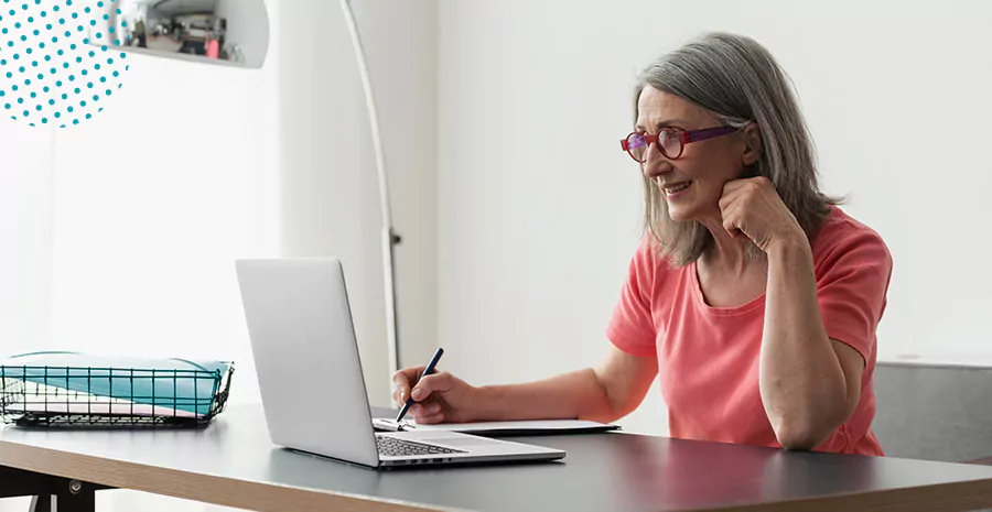 imagem de uma mulher sentada na frente de um computador escrevendo em um caderno