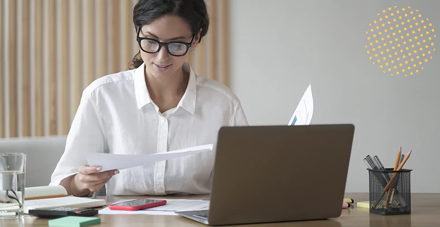 imagem de uma mulher sentada na frente de um computador segurando folhas de papel