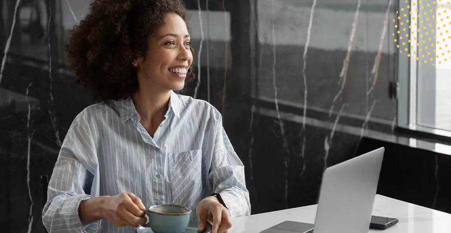 imagem de uma mulher sorrindo sentada na frente de um computador e segurando uma xícara