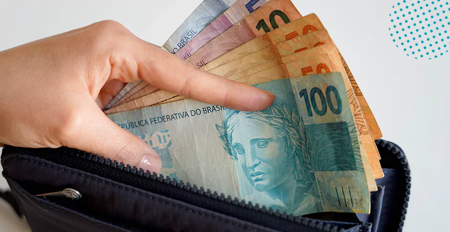 Uma mão tirando várias notas de reais de diferentes valores de uma carteira