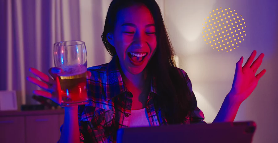 Uma jovem com uma cerveja na mão sorrindo para o notebook