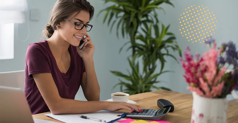 Uma mulher falando ao celular enquanto utiliza uma calculadora