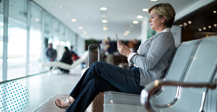 Um mulher sentada em um banco de aeroporto mexendo em um celular.