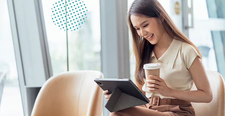 Uma mulher sorrindo enquanto usa um tablet e toma tum café