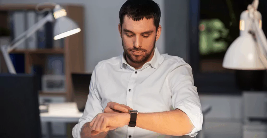 Homem olhando para relógio de pulso com escritório ao fundo