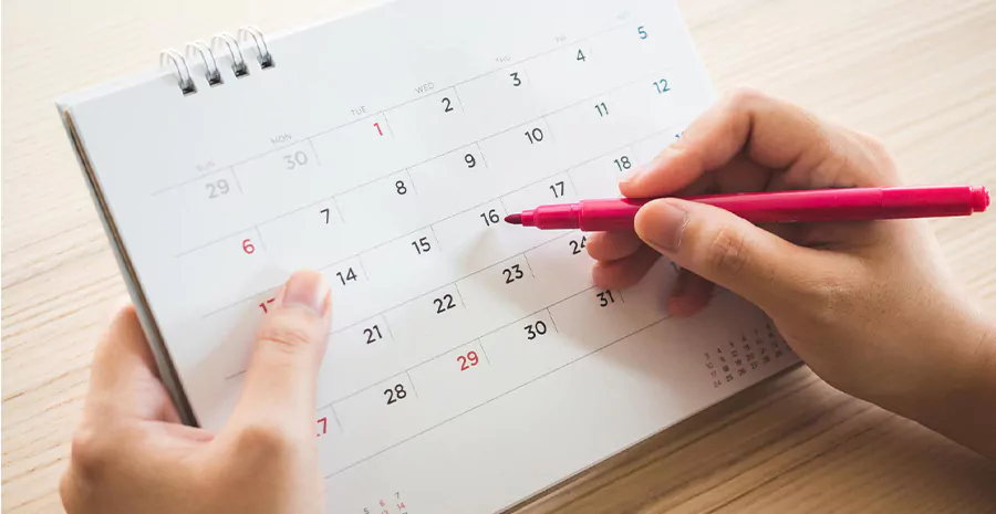 imagem de uma pessoa segurando um calendário com uma caneta para riscar uma data