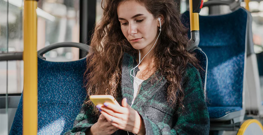 Mulher em um ônibus sentada com fones e observando seu celular