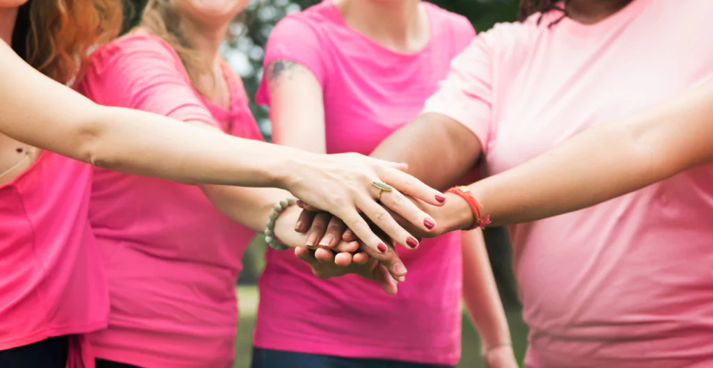 Várias mulheres de rosa sobrepondo as suas mãos