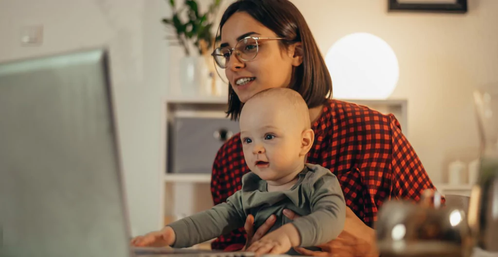Mulher segurando um bebe em frente a um computador