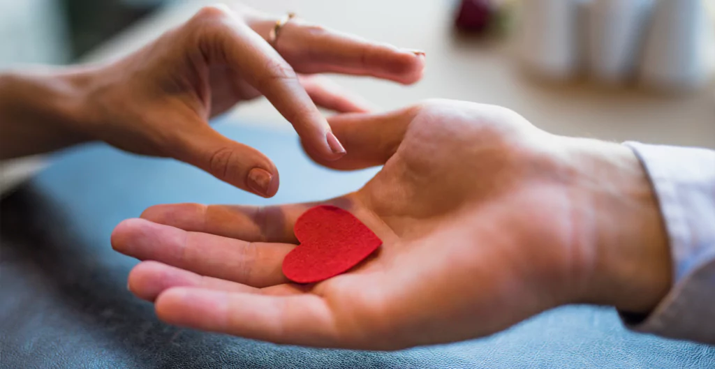 Mão segurando um papel em formato de coração vermelho