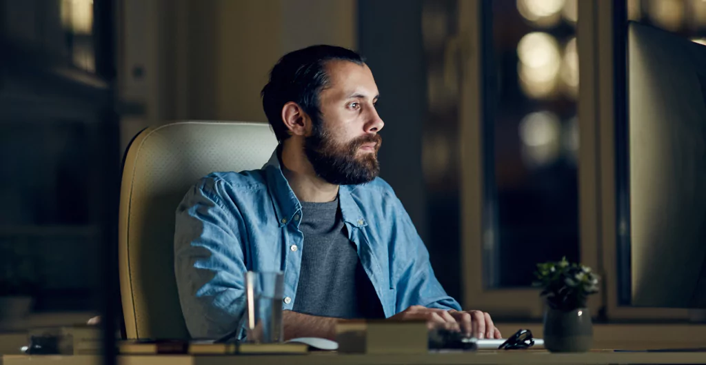 Homem sentado na mesa em quarto escuro com computador