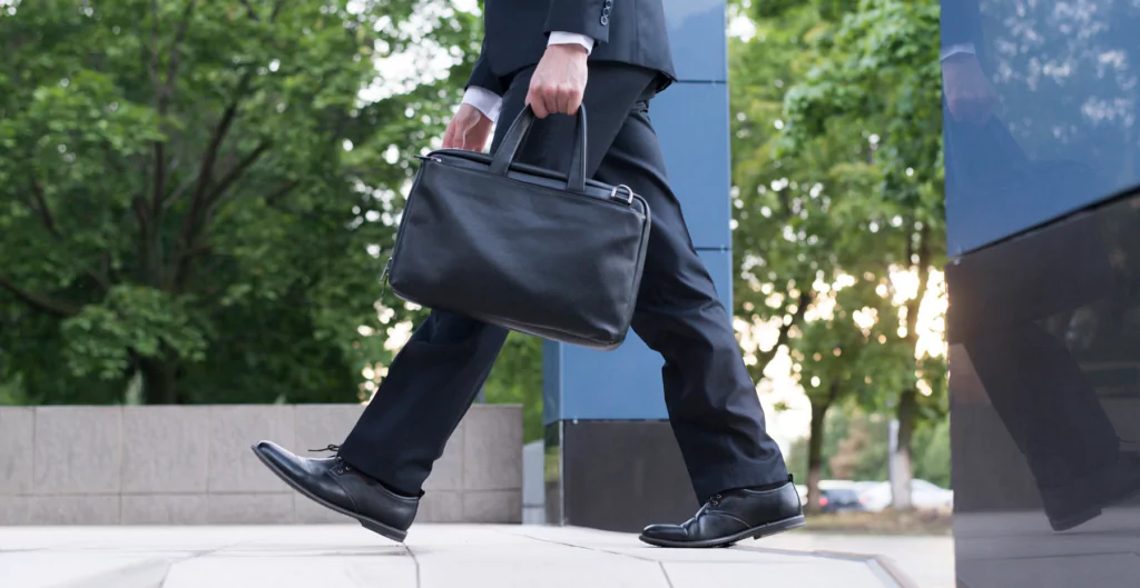 Executivo em traje formal andando na calçada segurando uma maleta