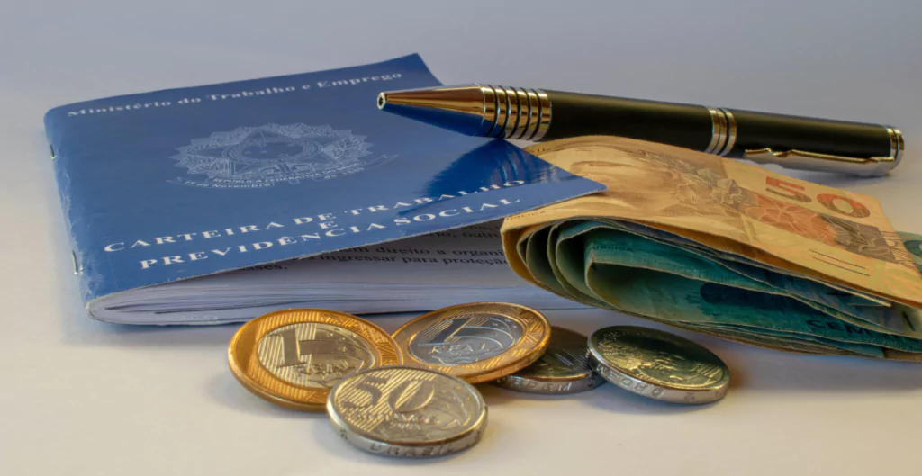 Uma carteira de trabalho, caneta, moedas e dinheiro em uma mesa