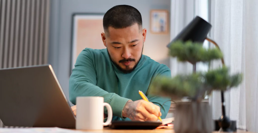 Um homem sentado em uma mesa com um laptop e uma caneta
