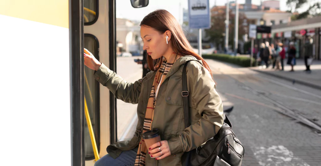 mulher com um fone de ouvido e segurando um café subindo no ônibus